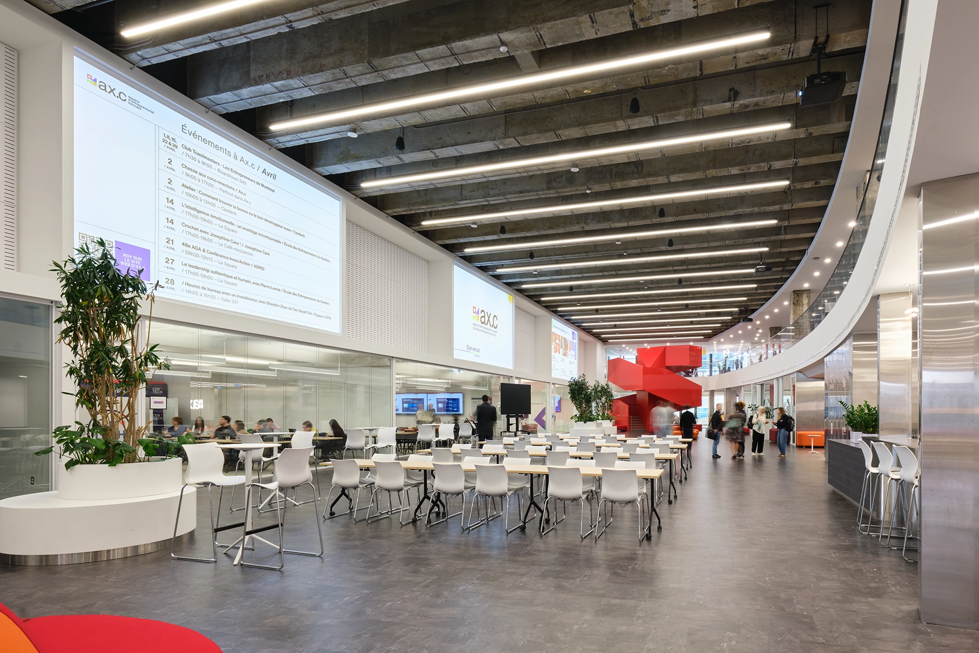 A workshop and event space at Ax.c, set with rows of tables and chairs under a concrete ceiling